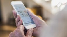 A close-up of a person holding a smartphone displaying heart rate and blood pressure data